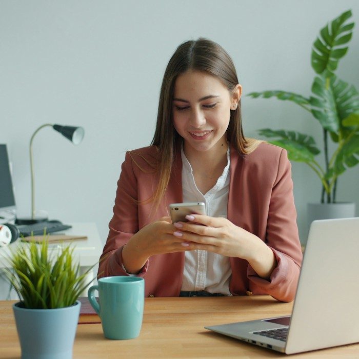 Pessoa sorrindo enquanto usa o celular no escritório